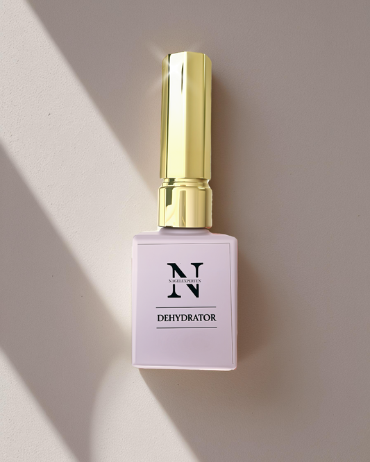 Lila flaska med guldig kork som glänser, innehållande dehydrator för avfettning av naglar. Bakgrunden är beige med skuggor från fönster.