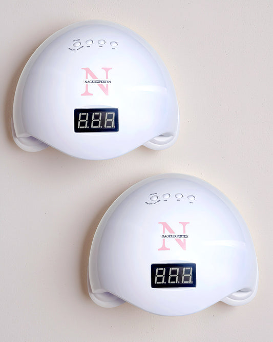 Två vita nagellampor från Nagelexperten för härdning av nagelprodukter som står på ett vitt bord.