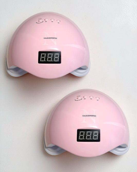 Två rosa uv-lampor från Nagelexperten som står på ett vitt bord.