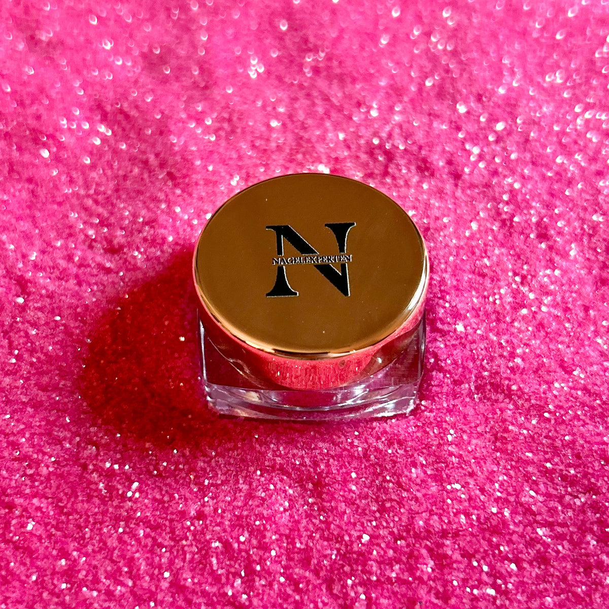 Burk med roseguldigt lock och rosa nagelglitter i bakgrunden.