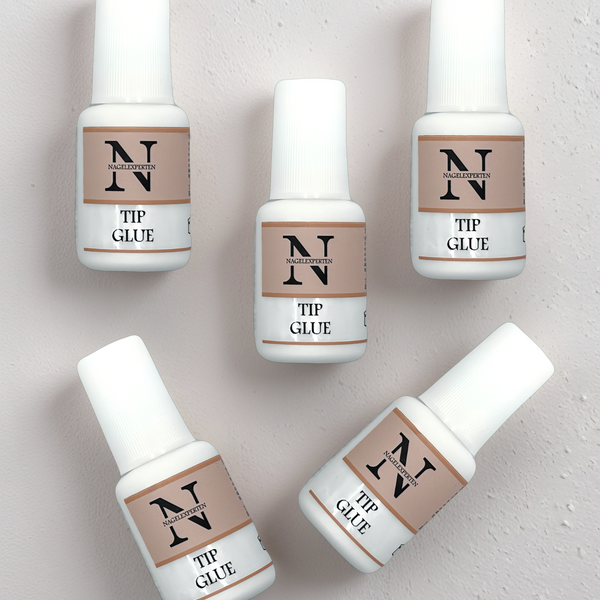 5 stycken nagellim med pensel liggandes på ett beige bord.